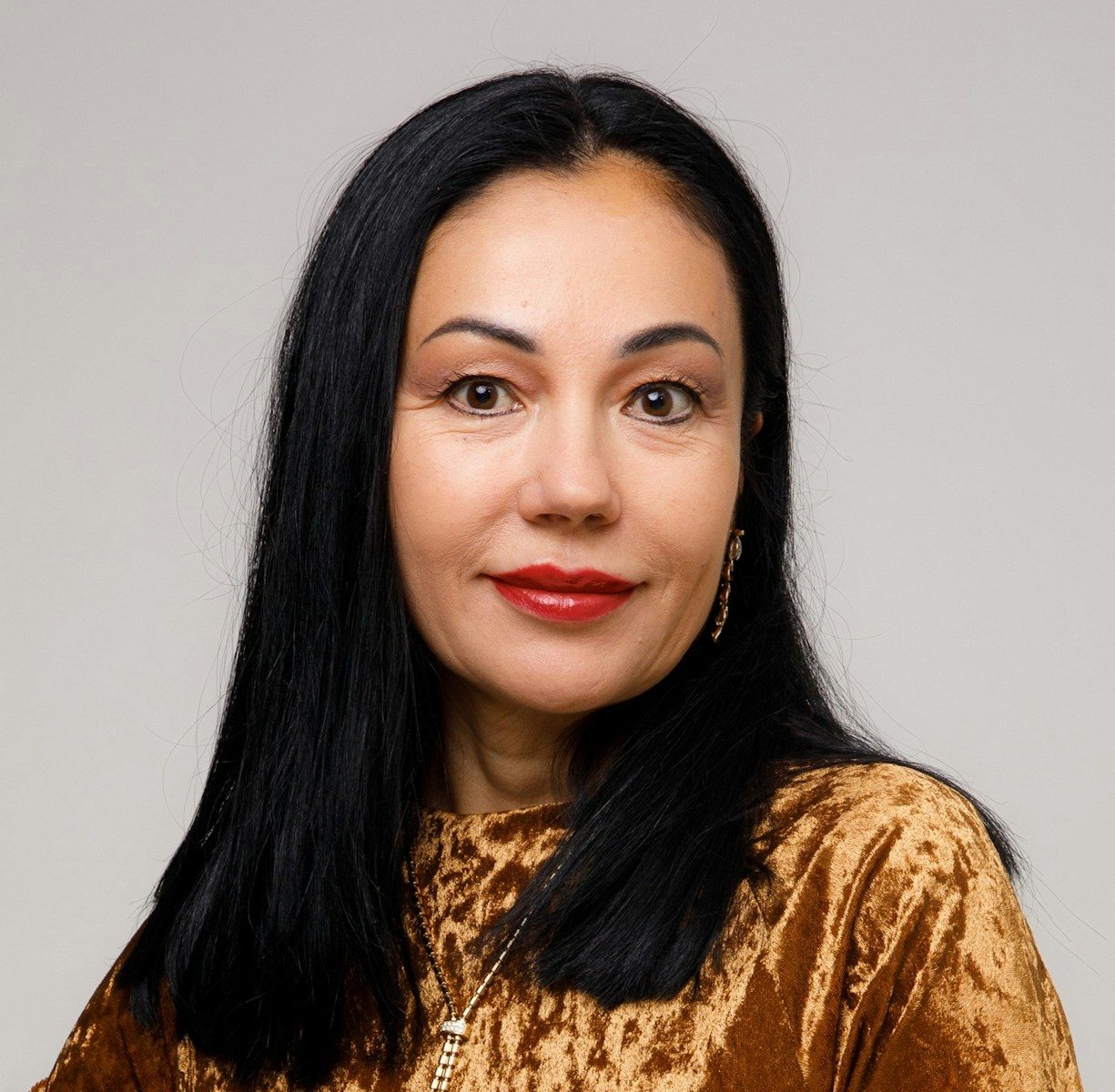 a woman with long black hair wearing a gold top